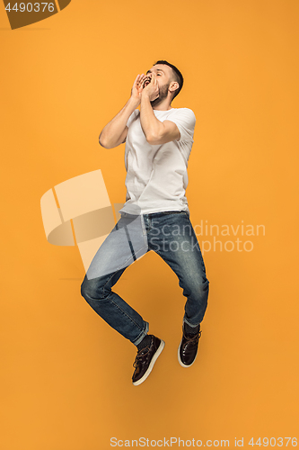 Image of Freedom in moving. handsome young man jumping against orange background