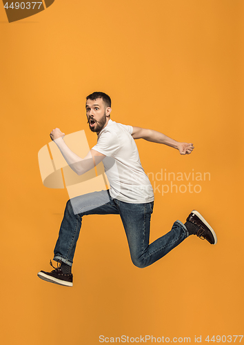 Image of Freedom in moving. handsome young man jumping against orange background