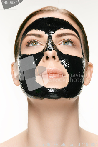 Image of Young beautiful woman applying a mask for the face of the therapeutic black mud. Spa treatment