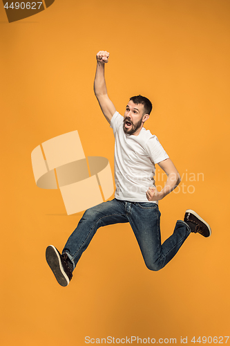 Image of Freedom in moving. handsome young man jumping against orange background