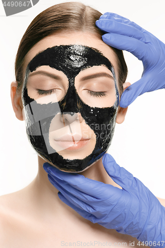 Image of Young beautiful woman applying a mask for the face of the therapeutic black mud. Spa treatment