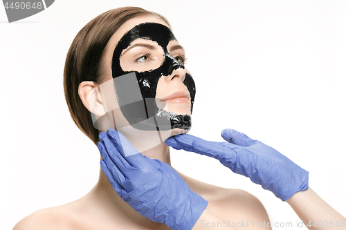 Image of Young beautiful woman applying a mask for the face of the therapeutic black mud. Spa treatment