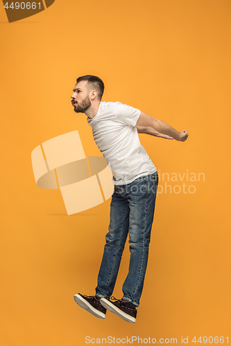 Image of Freedom in moving. handsome young man jumping against orange background