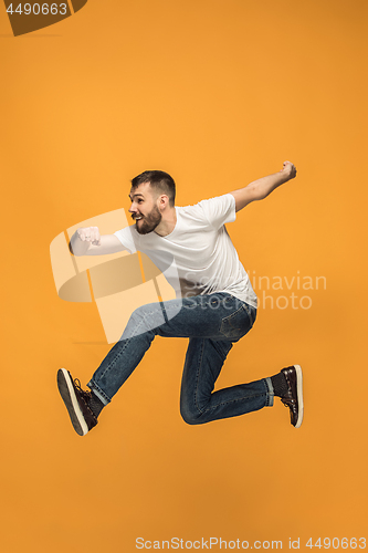 Image of Freedom in moving. handsome young man jumping against orange background