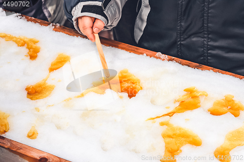 Image of Child putting maple taffy on a wooden stick 