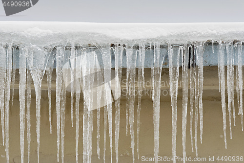 Image of Big icicles hang from the roof of a house.