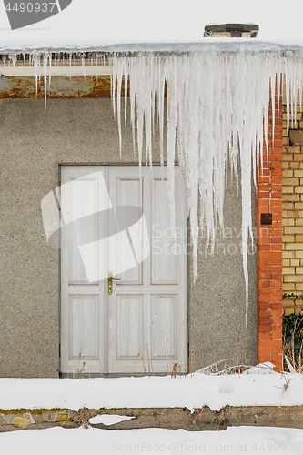 Image of Huge icicles hang from the roof of an abandoned house with wooden door