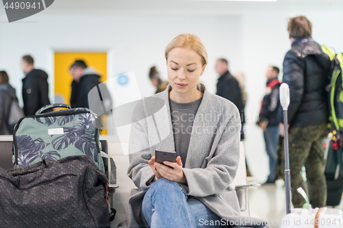 Image of Female traveler using her cell phone while waiting to board a plane at departure gates at airport terminal.