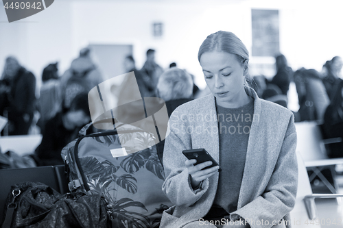 Image of Female traveler reading on her cell phone while waiting to board a plane at departure gates at airport terminal.