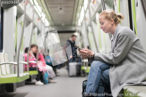 Image of Beautiful blonde woman wearing winter coat reading on the phone while traveling by metro public transport.