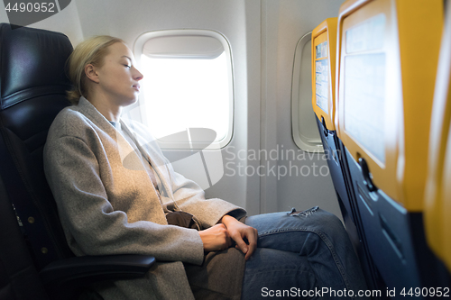 Image of Woman napping on seat while traveling by airplane.