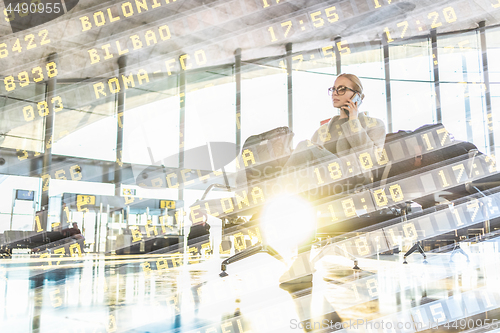 Image of Female traveler talking on her cell phone while waiting to board a plane at departure gates at airport terminal.