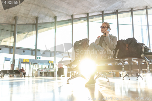 Image of Female traveler talking on her cell phone while waiting to board a plane at departure gates at airport terminal.