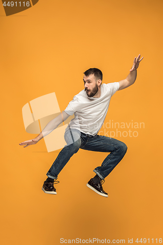 Image of Freedom in moving. handsome young man jumping against orange background