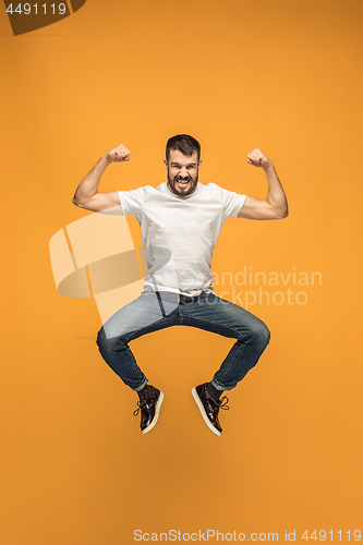 Image of Freedom in moving. handsome young man jumping against orange background