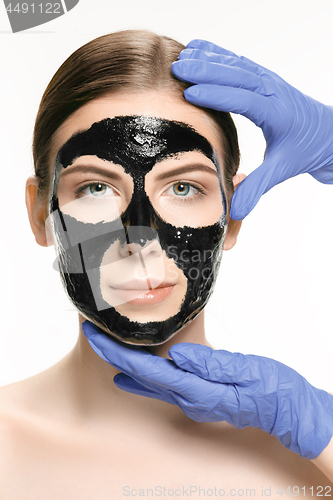 Image of Young beautiful woman applying a mask for the face of the therapeutic black mud. Spa treatment