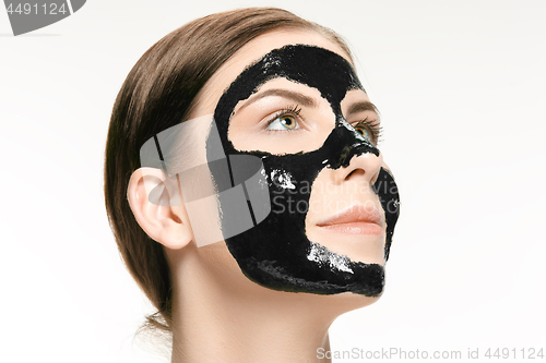 Image of Young beautiful woman applying a mask for the face of the therapeutic black mud. Spa treatment