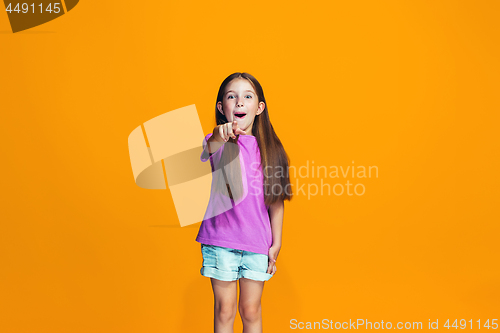 Image of The happy teen girl pointing to you, half length closeup portrait on orange background.