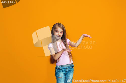 Image of The happy teen girl presenting something, half length closeup portrait on orange background.