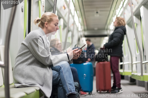 Image of Beautiful blonde woman wearing winter coat reading on the phone while traveling by metro public transport.