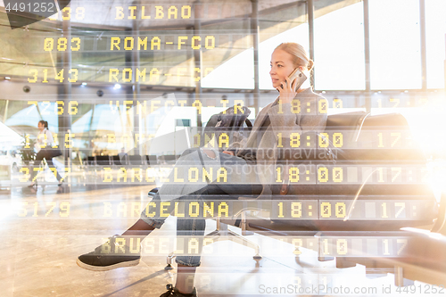 Image of Female traveler talking on her cell phone while waiting to board a plane at departure gates at airport terminal.