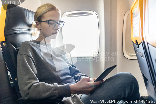 Image of Woman wearing glasses reading on digital e-reader while traveling by airplane.