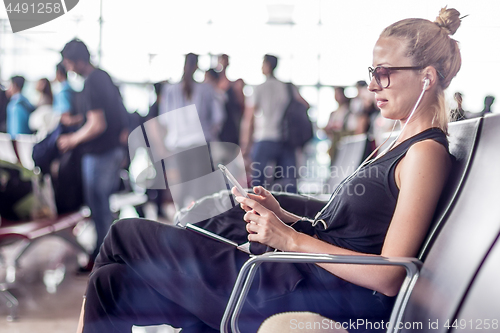 Image of Female traveler using her cell phone while waiting to board a plane at departure gates at asian airport terminal.