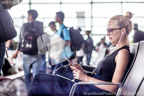 Image of Female traveler using her cell phone while waiting to board a plane at departure gates at asian airport terminal.