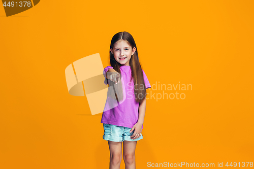 Image of The happy teen girl pointing to you, half length closeup portrait on orange background.