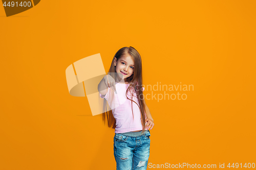 Image of The happy teen girl pointing to you, half length closeup portrait on orange background.