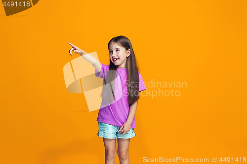 Image of The happy teen girl pointing to you, half length closeup portrait on orange background.