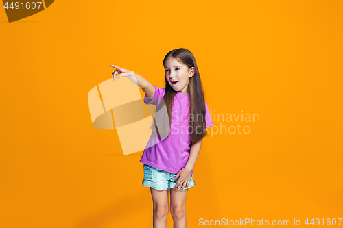 Image of The happy teen girl pointing to you, half length closeup portrait on orange background.