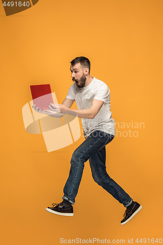 Image of Image of young man over orange background using laptop computer while jumping.