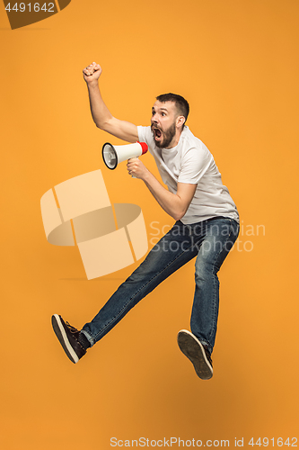 Image of Jumping fan on orange background. The young man as soccer football fan with megaphone