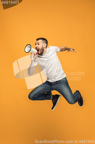 Image of Jumping fan on orange background. The young man as soccer football fan with megaphone