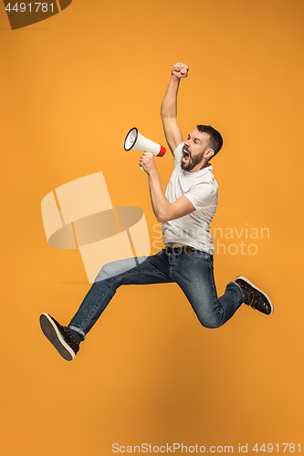 Image of Jumping fan on orange background. The young man as soccer football fan with megaphone