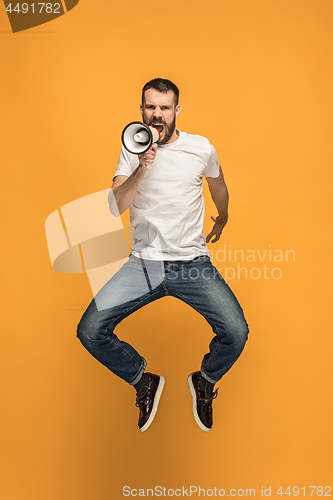 Image of Jumping fan on orange background. The young man as soccer football fan with megaphone