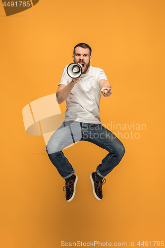 Image of Jumping fan on orange background. The young man as soccer football fan with megaphone