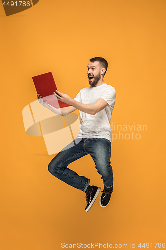 Image of Image of young man over orange background using laptop computer while jumping.