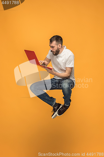 Image of Image of young man over orange background using laptop computer while jumping.
