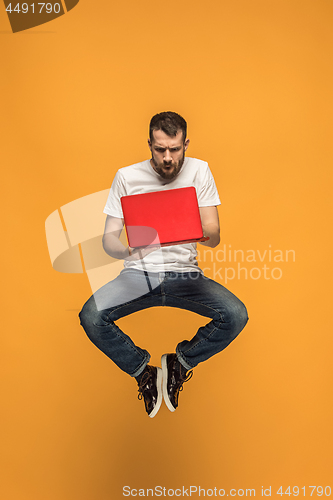 Image of Image of young man over orange background using laptop computer while jumping.