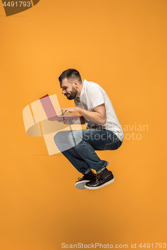 Image of Image of young man over orange background using laptop computer while jumping.