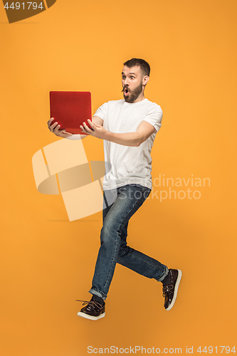 Image of Image of young man over orange background using laptop computer while jumping.