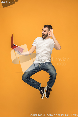 Image of Image of young man over orange background using laptop computer while jumping.