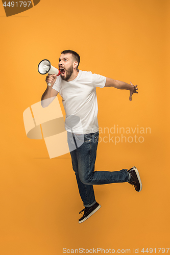 Image of Jumping fan on orange background. The young man as soccer football fan with megaphone