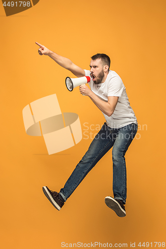 Image of Jumping fan on orange background. The young man as soccer football fan with megaphone