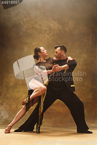 Image of Dance ballroom couple in gold dress dancing on studio background.