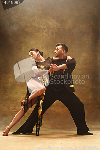 Image of Dance ballroom couple in gold dress dancing on studio background.