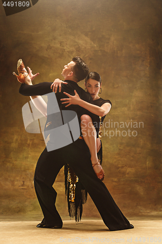 Image of Dance ballroom couple in gold dress dancing on studio background.