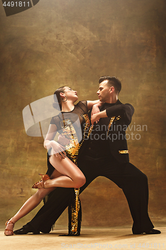 Image of Dance ballroom couple in gold dress dancing on studio background.